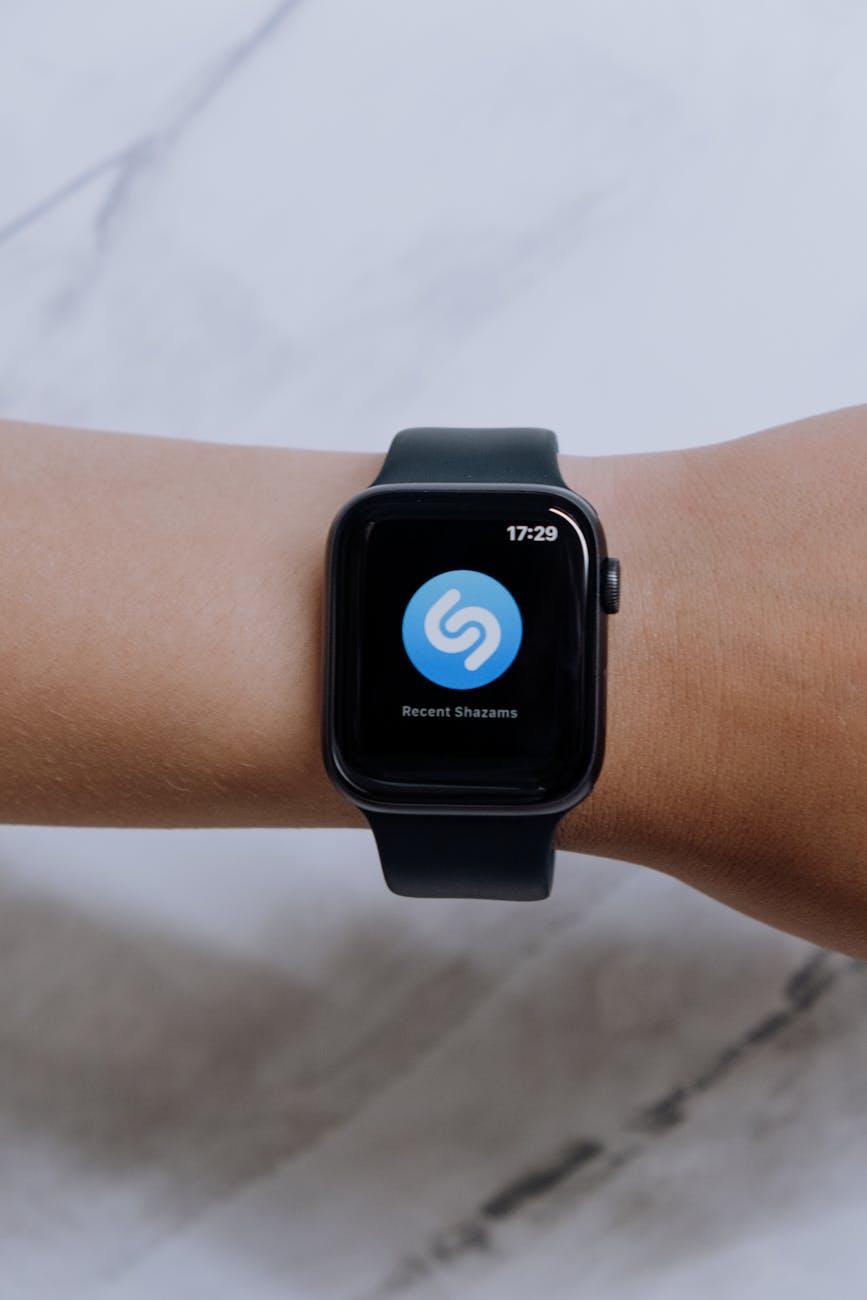 A digital smartwatch displaying a music recognition app on a person's wrist with a marble background.