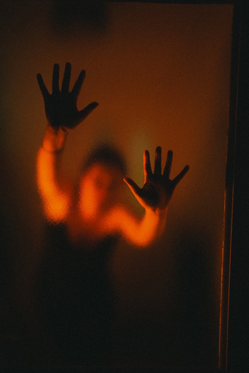 Silhouette of a woman pressing hands against frosted glass with dramatic lighting.