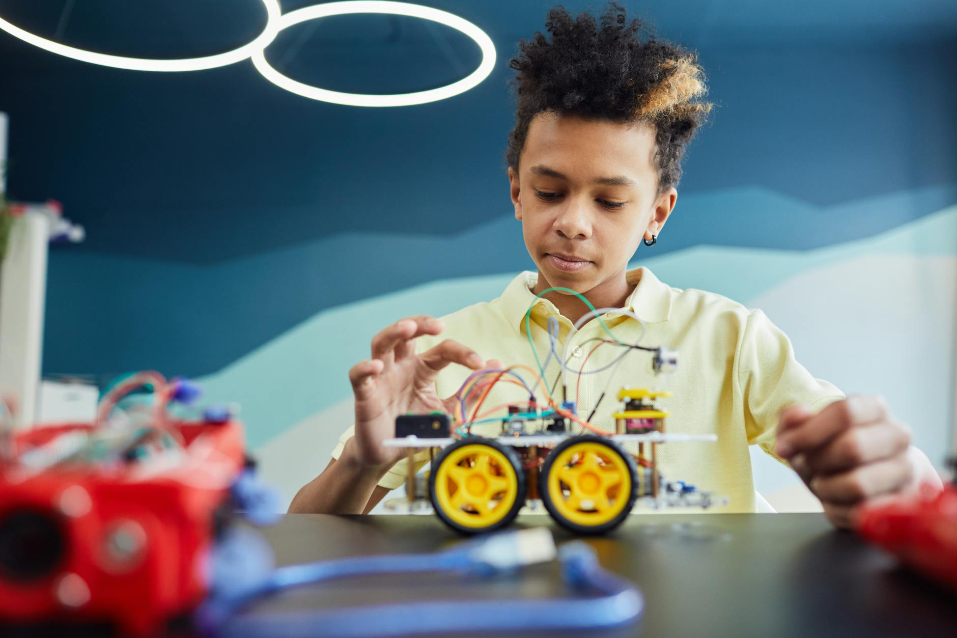 Boy explores robotics with toy vehicle and wires in a classroom setting.